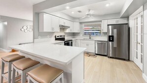 A modern kitchen with white cabinetry, a central island with stools, stainless steel appliances, and a ceiling fan.