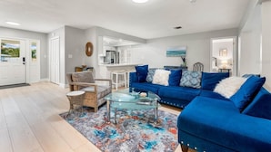 A modern living room with a blue sofa, a glass coffee table, and a patterned rug.