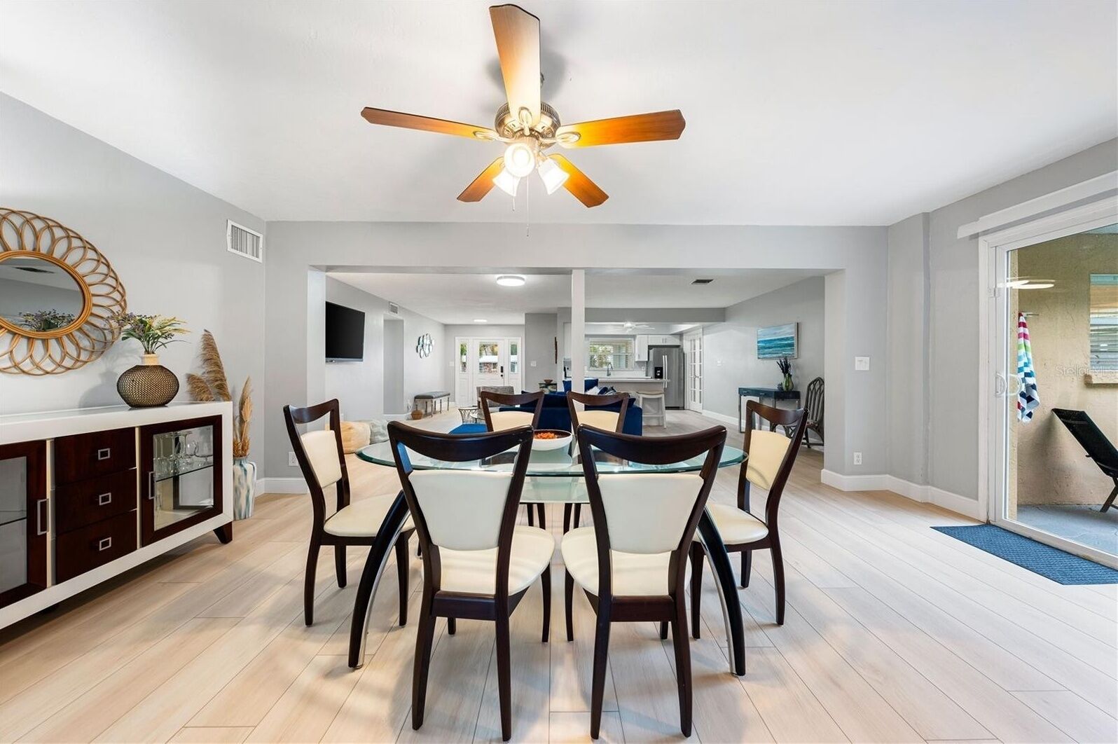 A modern dining area with a glass table, dark wooden chairs, and a ceiling fan.