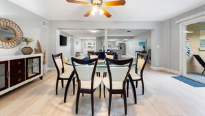 A modern dining area with a glass table, dark wooden chairs, and a ceiling fan.