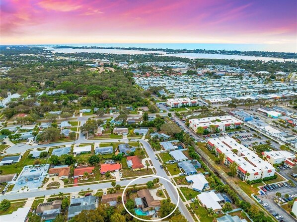 An aerial view of a residential area with a mix of single-family homes and commercial buildings, surrounded by greenery and a body of water in the distance.