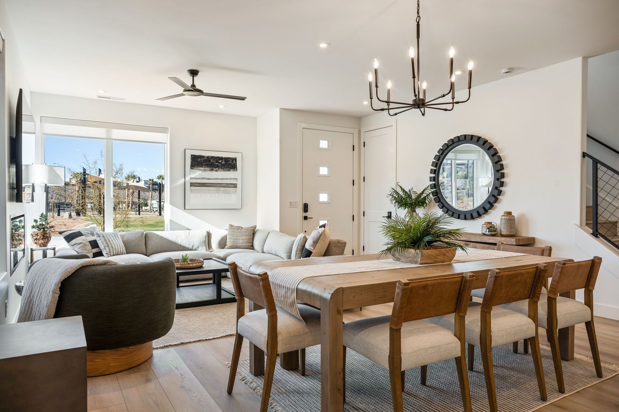 A spacious living room with a large sofa, a dining table with chairs, a chandelier, and a large mirror on the wall.