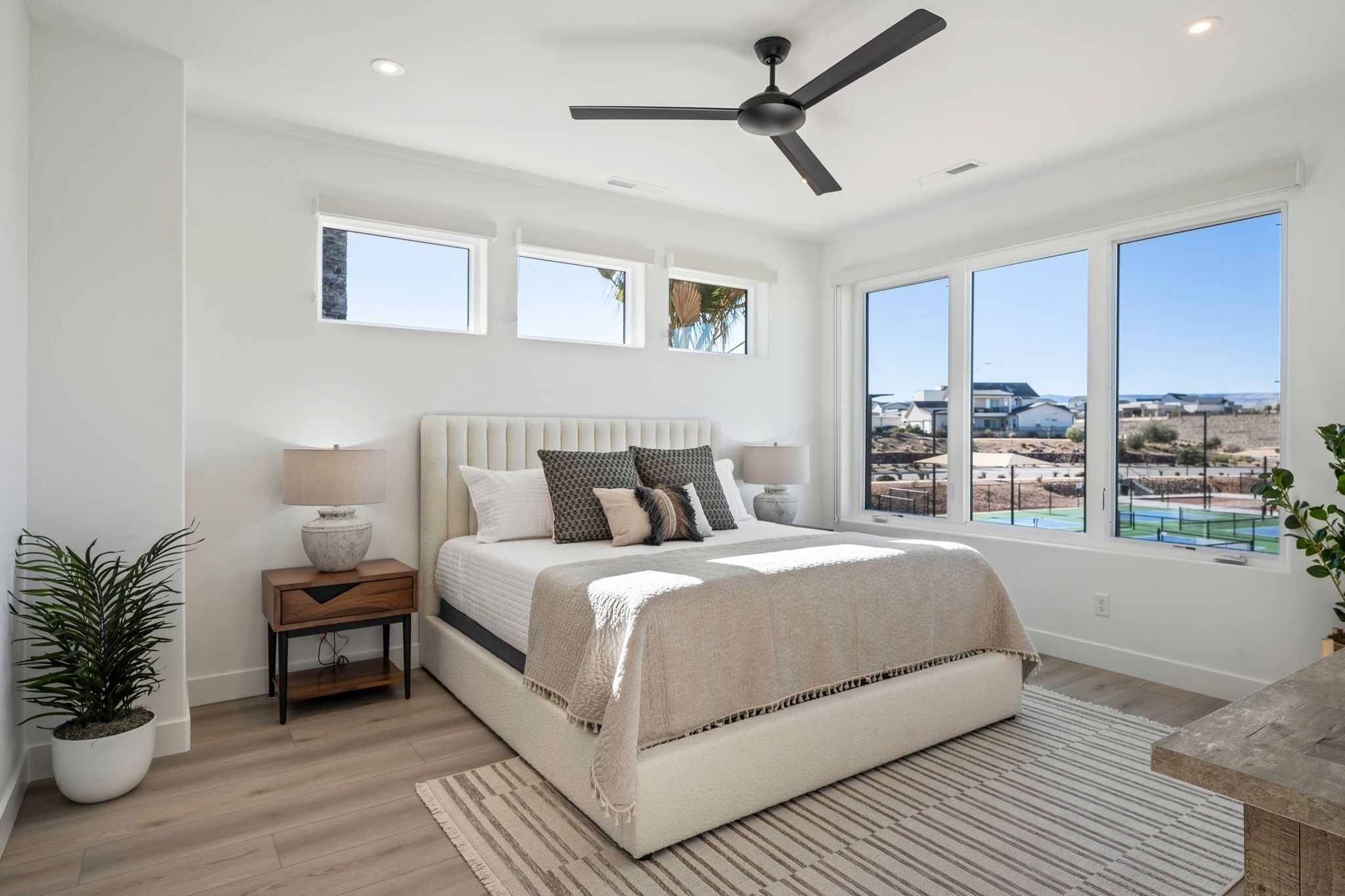 Ein Schlafzimmer mit einem großen Bett, einem Deckenventilator, Blick auf den Strand und einer Zimmerpflanze.
