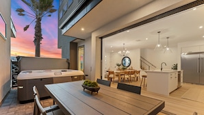 A modern kitchen with a central island, a dining area with a table and chairs, and a view of the sunset through the open space. - The Beach Club 5 Bedroom Home (St. George)