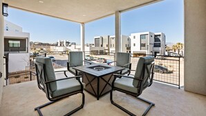 Un balcon avec une table et des chaises, une vue sur des immeubles modernes et un ciel dégagé.