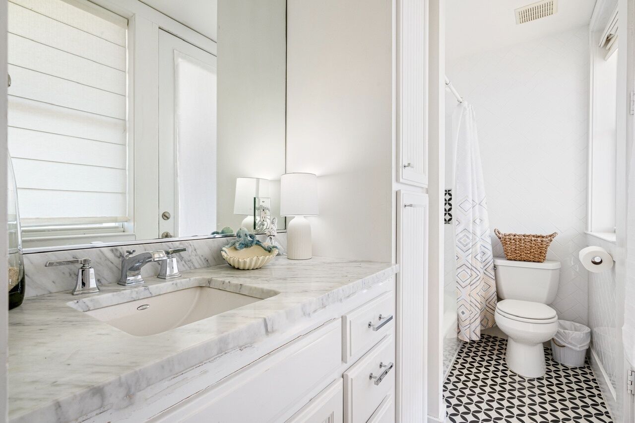 Une salle de bain avec un lavabo blanc, un miroir et des toilettes. Le sol est décoré de motifs et il y a un rideau de douche.