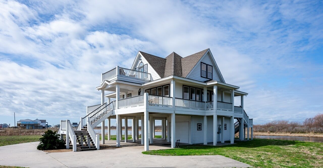 A large, two-story house with a balcony on the second floor, a covered porch, and a staircase leading to the upper level.