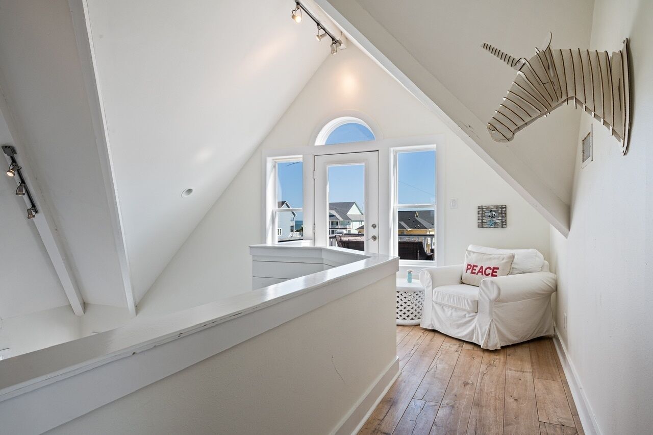 A white interior with a sloped ceiling, a white sofa with a 'PEACE' pillow, and a view of the outside through large windows.