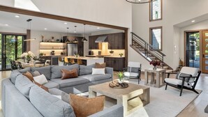 Un salon spacieux avec un grand canapé d’angle gris, une table basse et un escalier menant à l’étage supérieur.