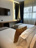 Habitación de hotel con cama, escritorio, televisor de pantalla plana en la pared y ventana con cortinas.