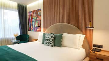 Una habitación de hotel con una cama grande, una mesita de noche con lámpara, una silla y un cuadro en la pared.