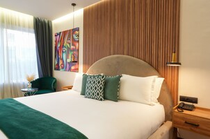 Una habitación de hotel con una cama grande, una mesita de noche con lámpara, una silla y un cuadro en la pared.
