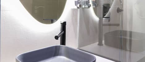 A modern bathroom with a large mirror, a rectangular sink, and a glass-enclosed shower area.