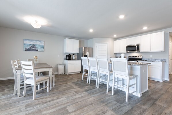A modern kitchen with white cabinetry, a dining area with white chairs, and a wooden floor.