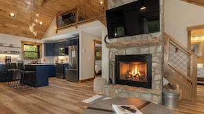 A spacious living area with a stone fireplace, wooden ceiling, and a kitchen with modern appliances.