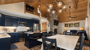 A modern kitchen with dark blue cabinets, a central island, and a stone fireplace. - In Boone! Hot Tub - Firepit - Sleeps 10 - Wifi (Boone)