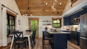 A modern kitchen with wooden beams, a central island, bar stools, and a dining area with a table and chairs. - In Boone! Hot Tub - Firepit - Sleeps 10 - Wifi (Boone)