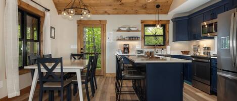 A modern kitchen with wooden beams, a central island, bar stools, and a dining area with a table and chairs.