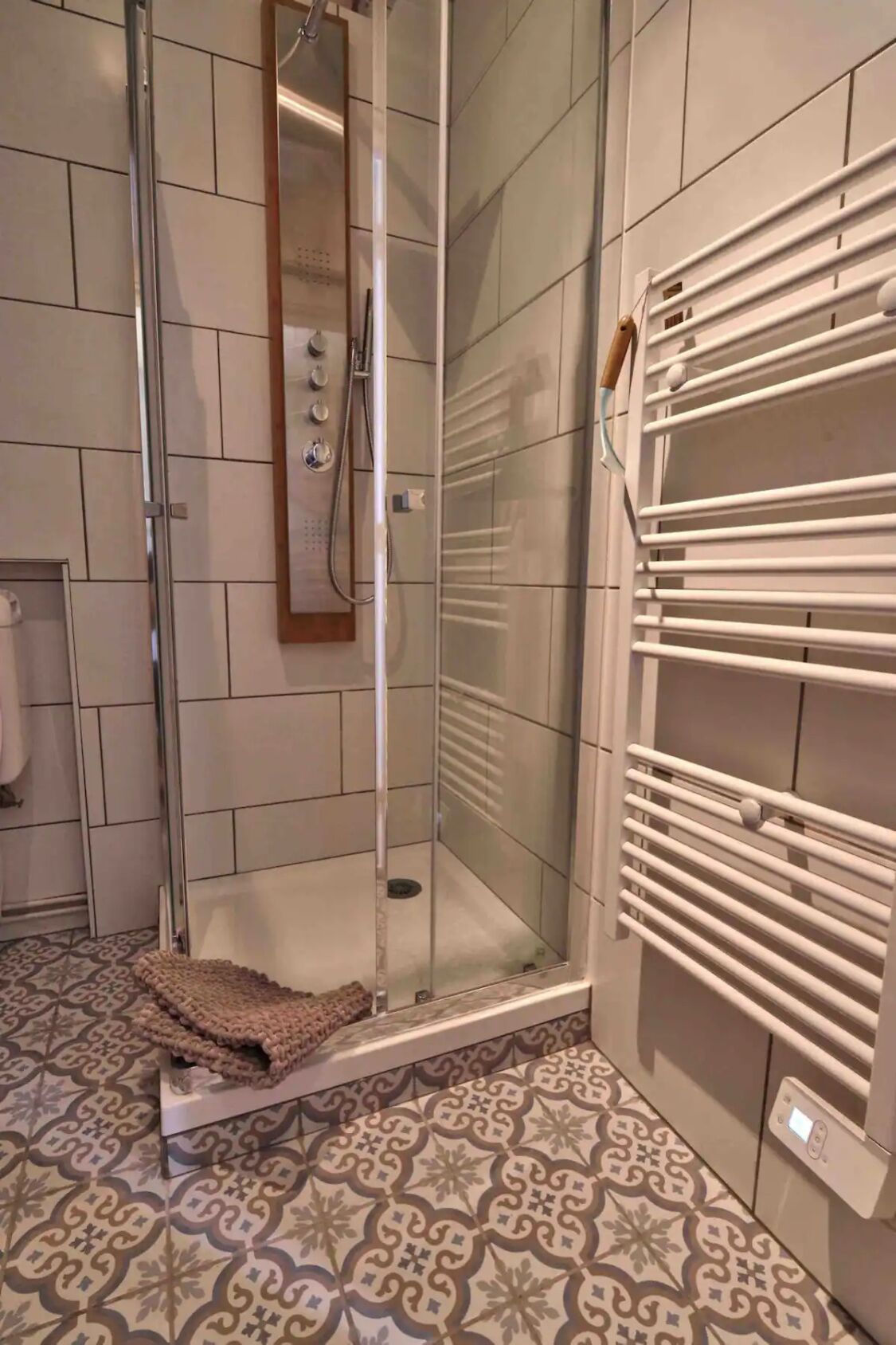 A shower area with a glass door, a towel rack, and patterned floor tiles.