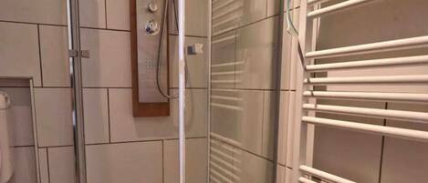 A shower area with a glass door, a towel rack, and patterned floor tiles.
