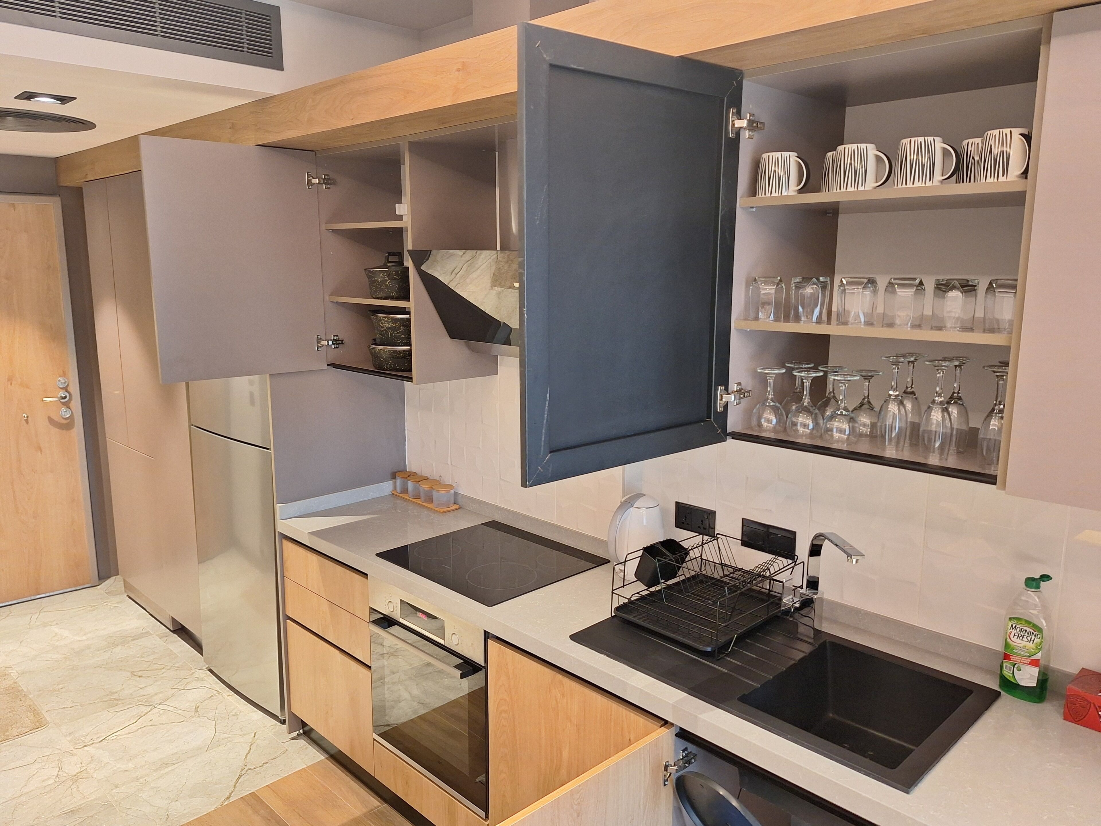 Una cocina moderna con armarios de madera, horno empotrado, un lavabo negro y una cafetera.