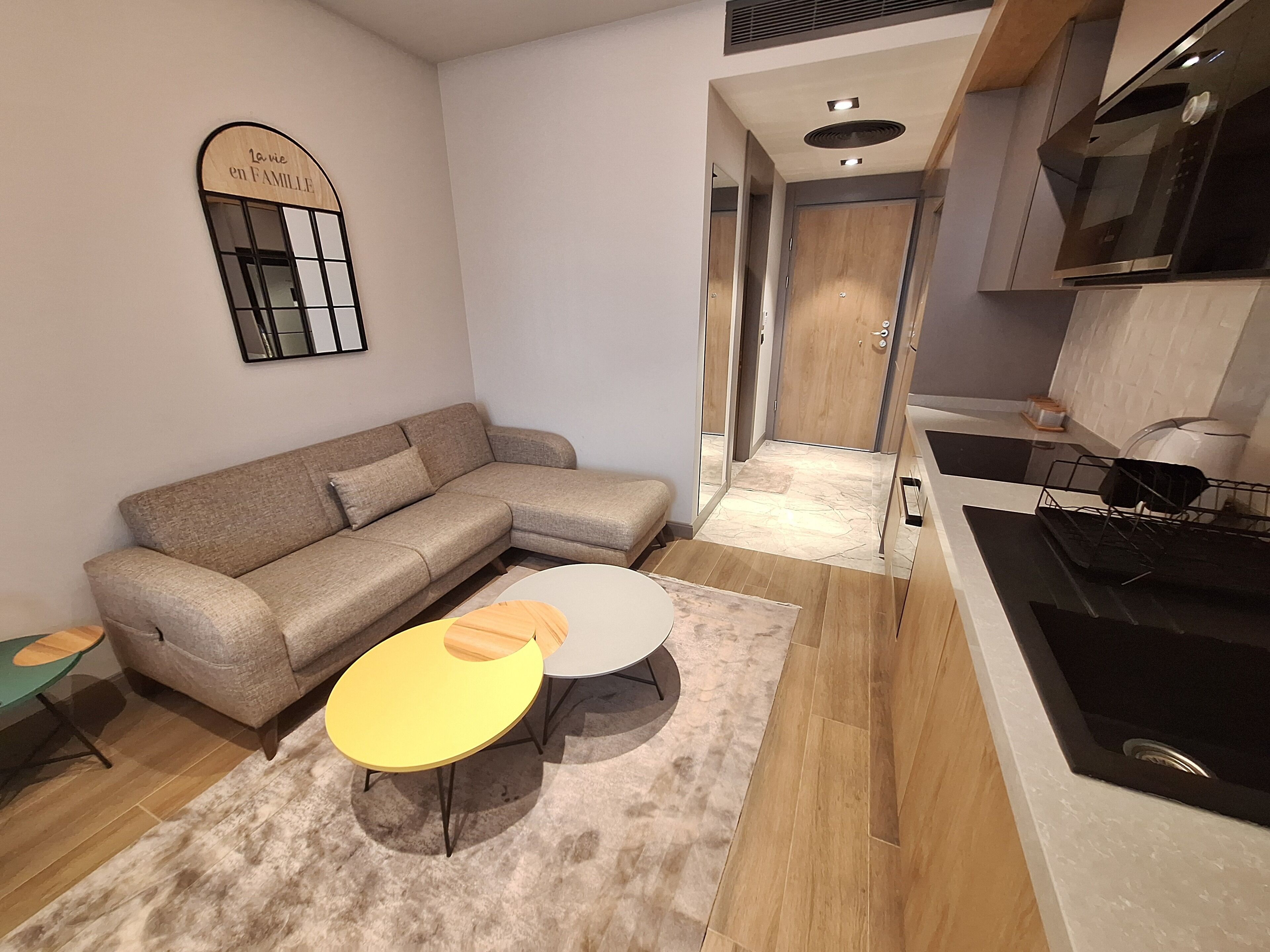 A modern living room with a sectional sofa, a small round table, and a kitchen area with a stove and microwave.