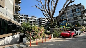 Un edificio moderno con balcones, un árbol y un coche rojo estacionado en la calle.