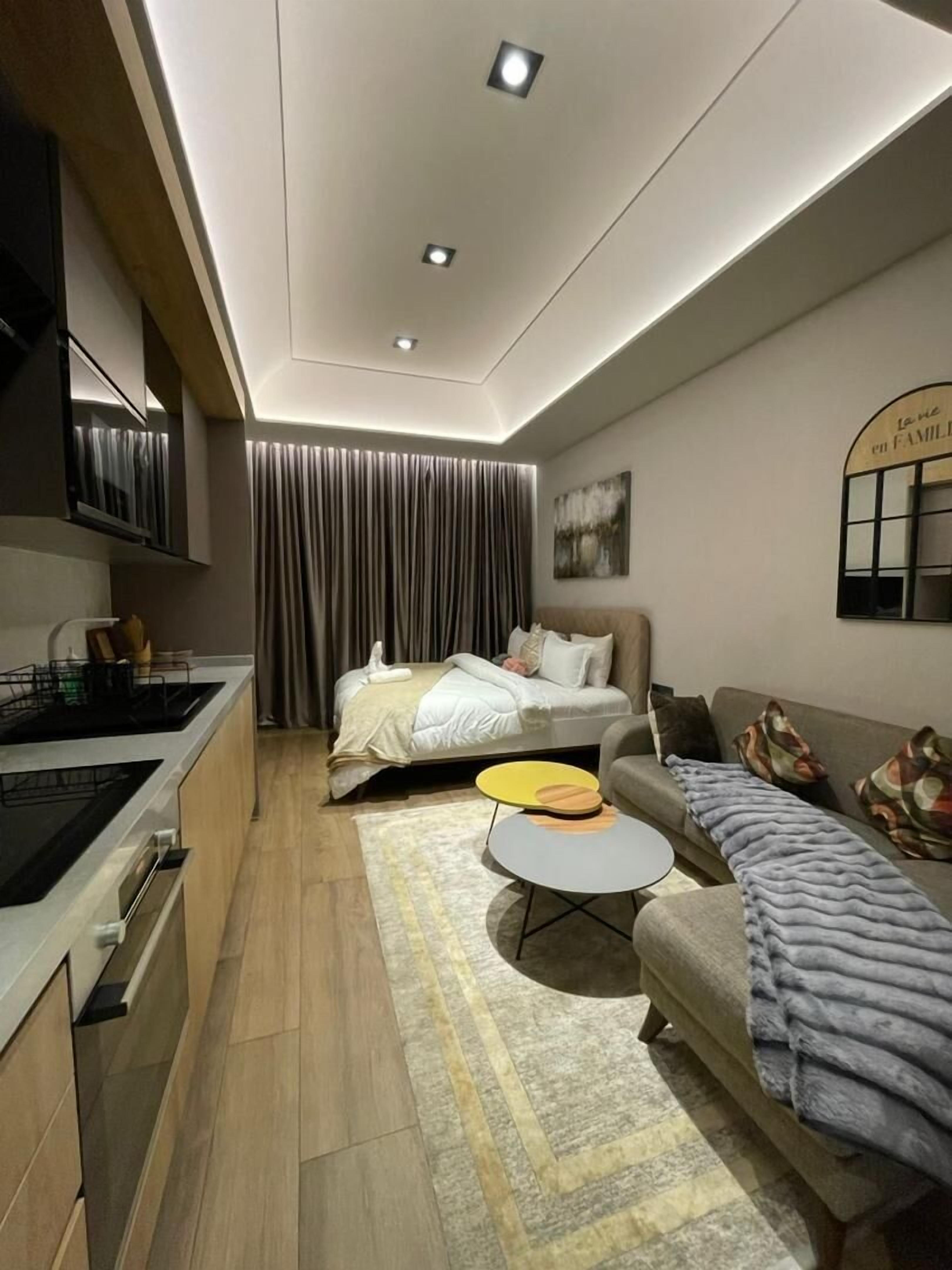A modern living room with a sofa, a coffee table, a bed, and a kitchen area.