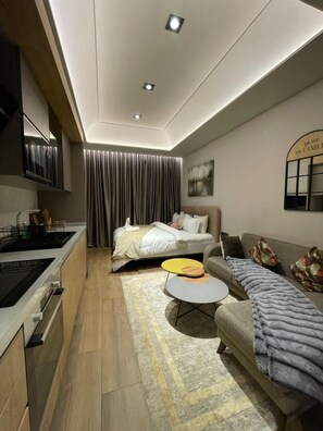 A modern living room with a sofa, a coffee table, a bed, and a kitchen area.