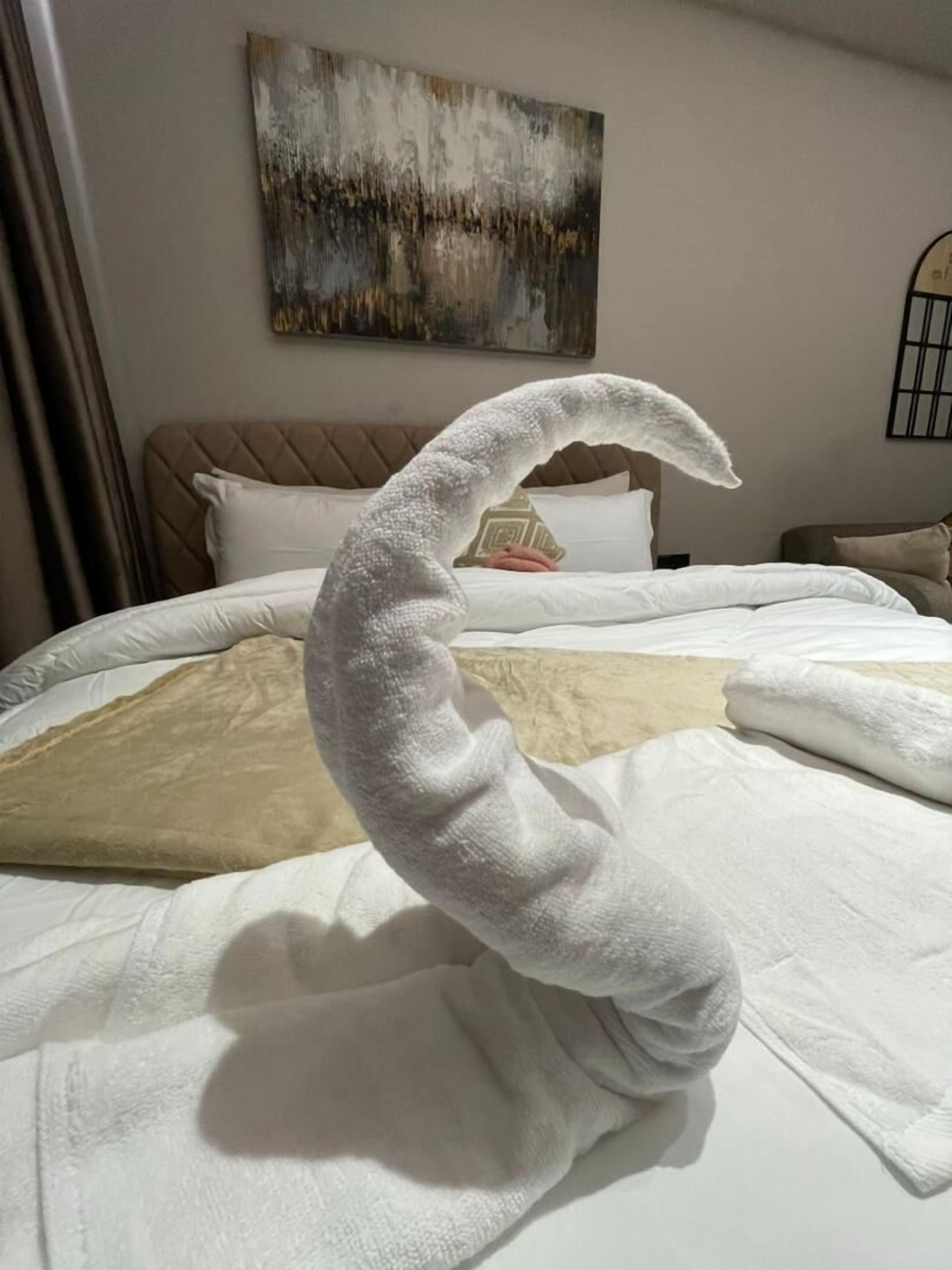 A bed with a white blanket and a towel shaped like a swan.