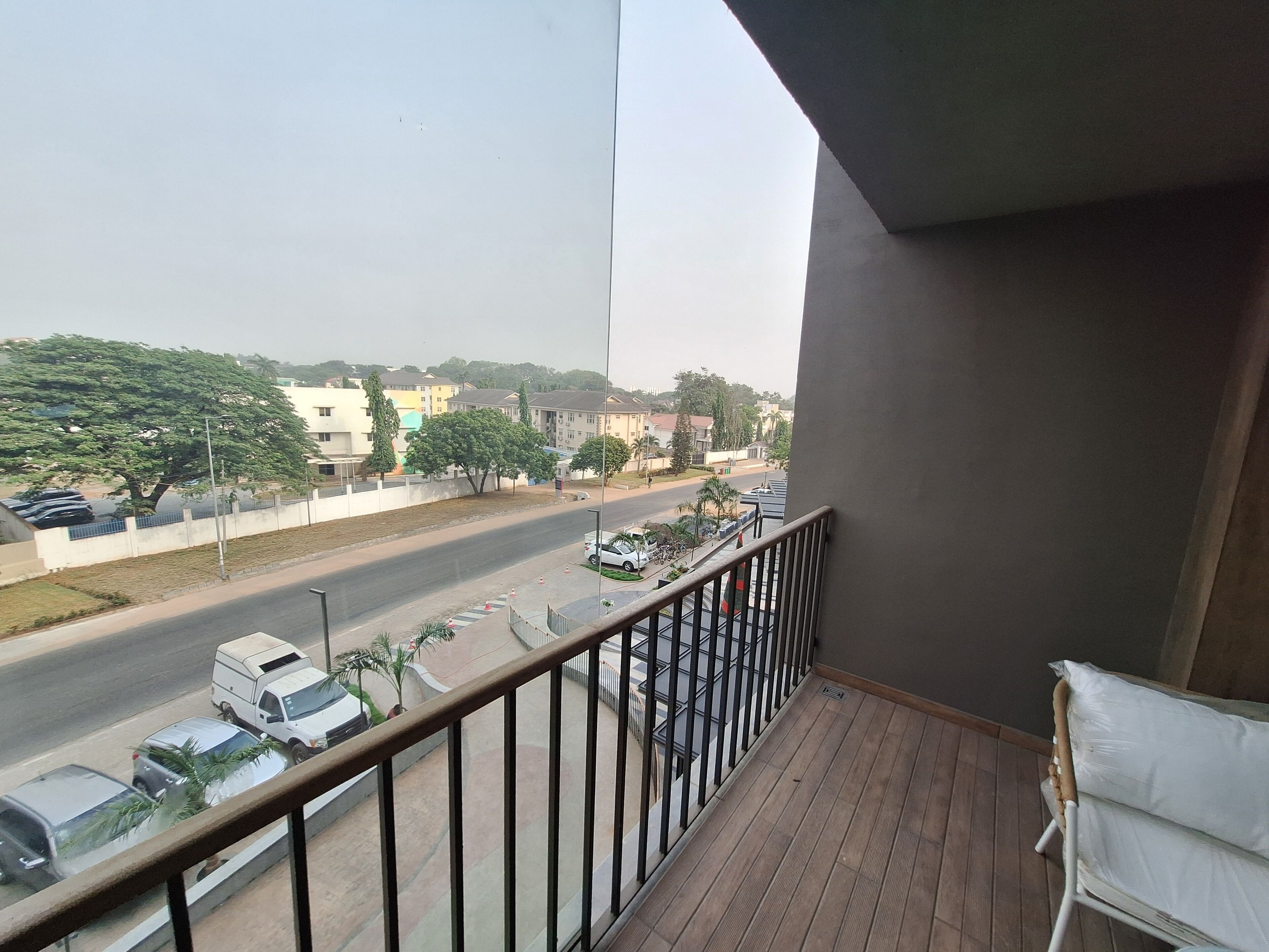 Un balcon donnant sur une route, des voitures garées et des bâtiments situés au loin.