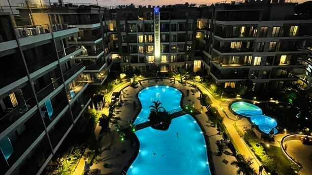 Un hotel de varios niveles con una piscina central, zonas de estar al aire libre y una fachada bien iluminada.