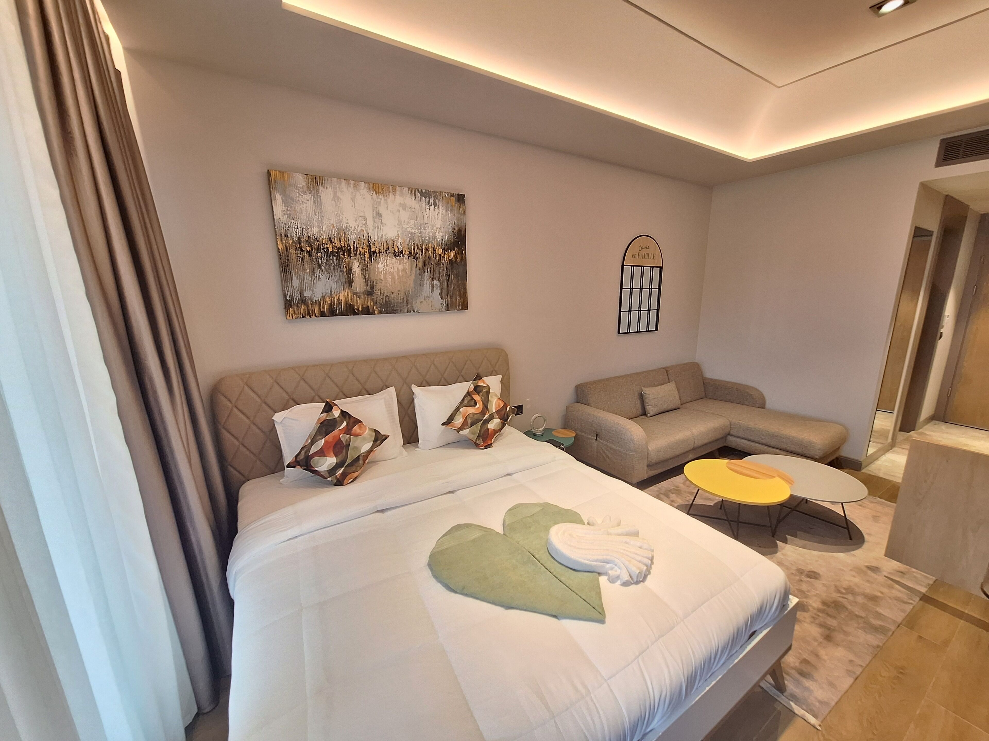 A modern hotel room with a large bed, a sofa, a small table, and a painting on the wall.