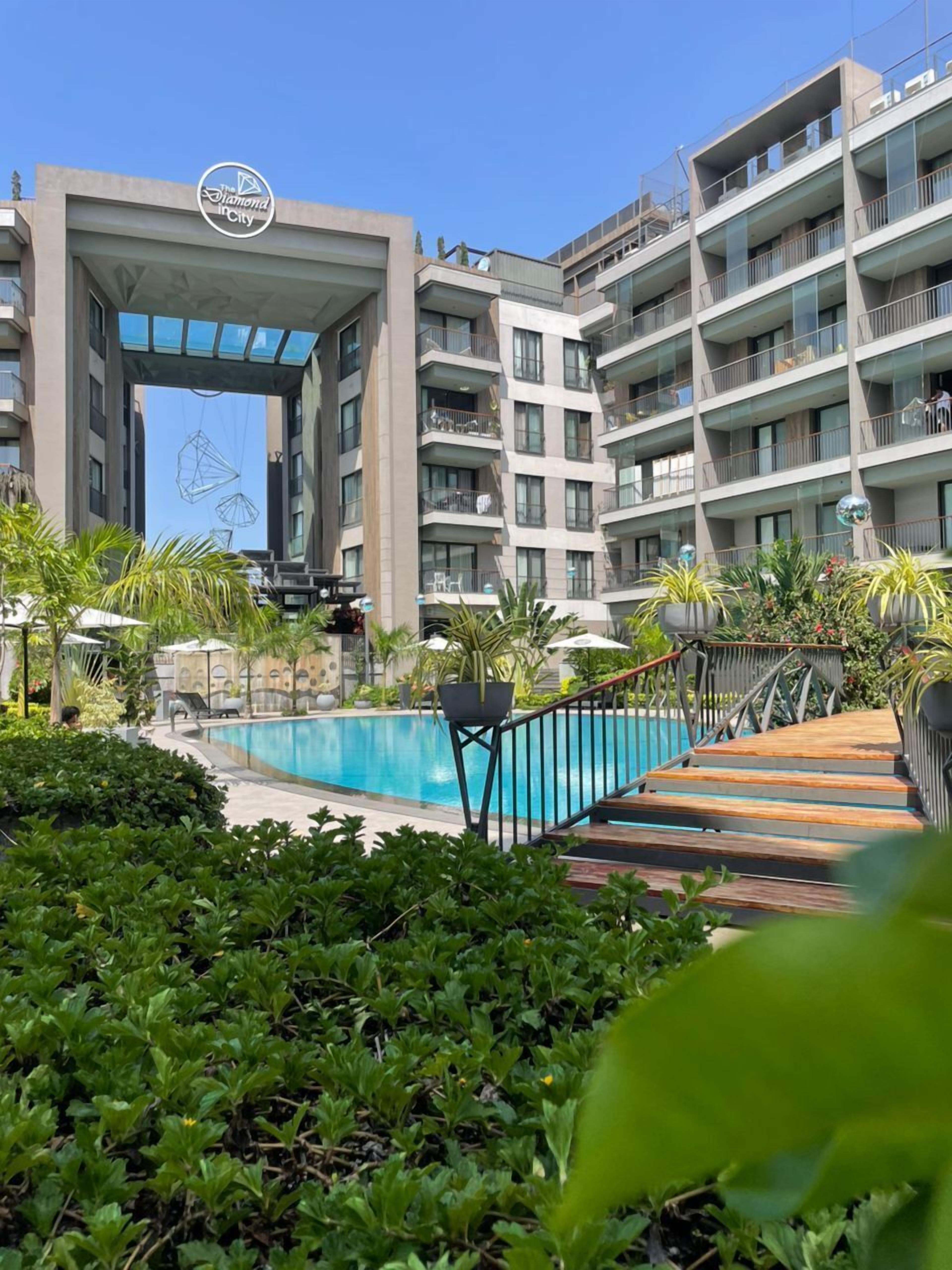Un hotel moderno con piscina, mobiliario exterior y entrada cubierta.
