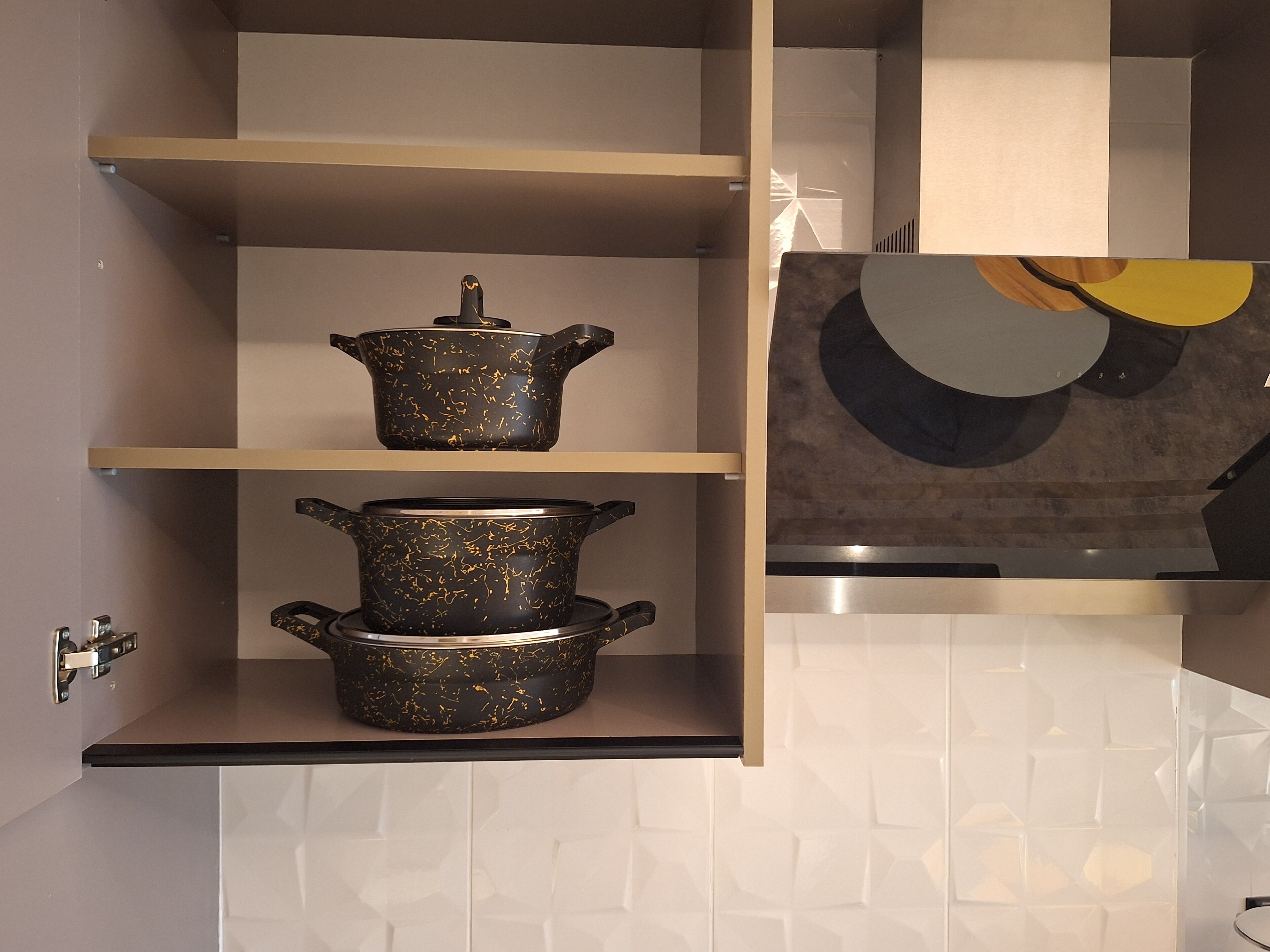 Une cuisine aux murs recouverts de carreaux blancs, deux pots noirs ornés de motifs dorés, placés sur des étagères, et une œuvre d’art moderne et abstraite accrochée au mur.