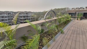 Una terraza en la azotea con cubierta de madera, rodeada de plantas en macetas y una estructura arquitectónica moderna.