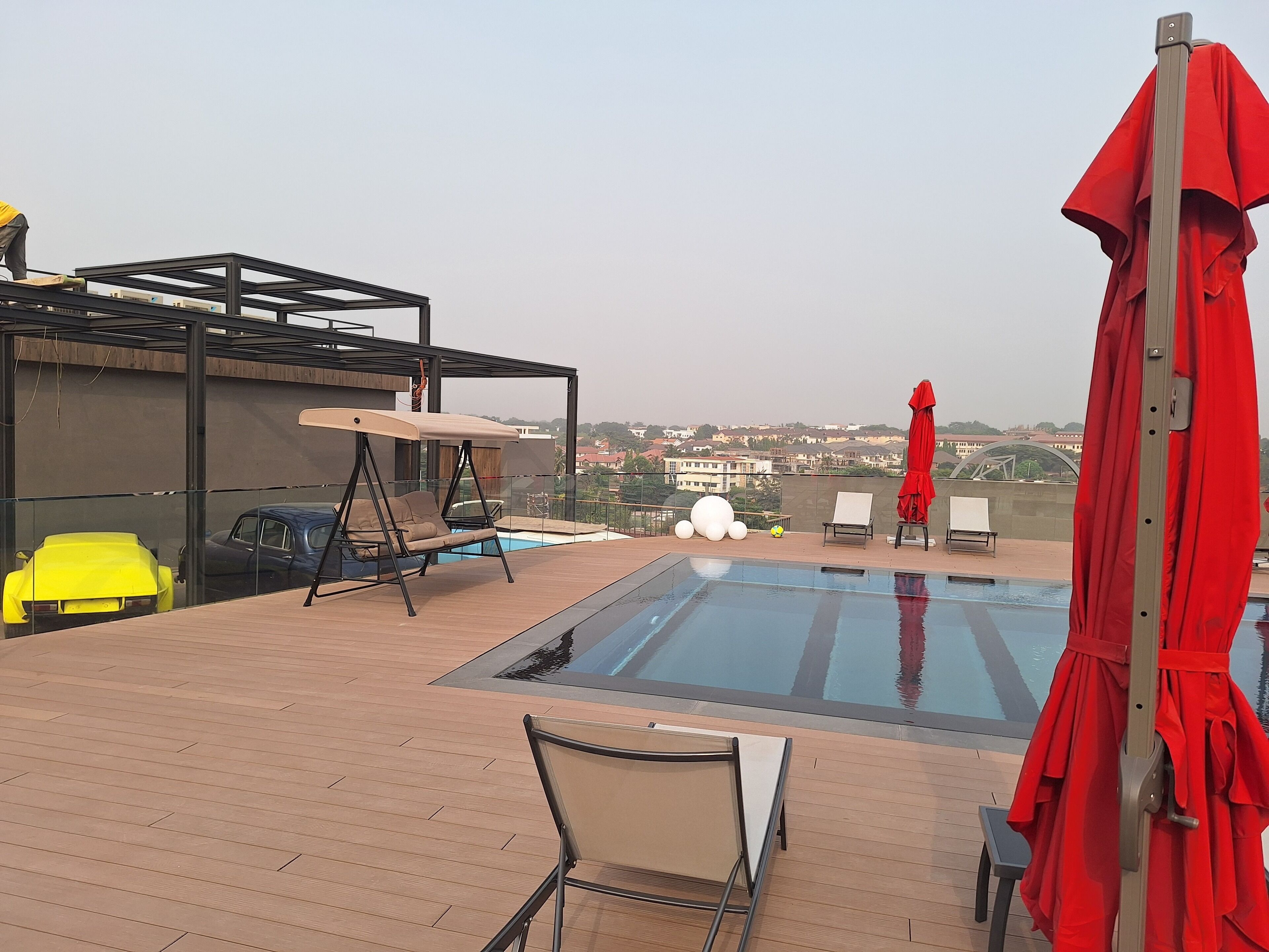 A rooftop pool area with a glass enclosure, a swing chair, and a red umbrella.