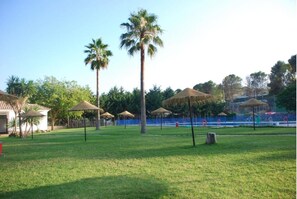 Relax under the shade of thatched umbrellas amidst lush greenery and a serene lawn.