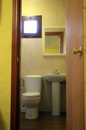 Bathroom with a pedestal sink and toilet, featuring a window above the sink.