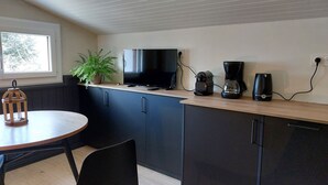 Eine kompakte Küche mit Holzarbeitsplatte, einem Fernseher, einer Kaffeemaschine und einem Blumentopf.
