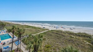 A beach with a pool area, palm trees, and a clear view of the ocean. - Oceanfront Crescent Beach 1K, 1Q, 1D, 2Tw, SS (North Myrtle Beach)