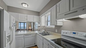 A modern kitchen with white cabinetry, a dishwasher, a double oven, and a large window providing natural light. - Oceanfront Crescent Beach 1K, 1Q, 1D, 2Tw, SS (North Myrtle Beach)