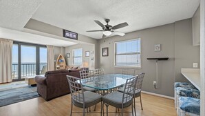 A spacious living room with a glass-top dining table, a brown sofa, and a ceiling fan. - Oceanfront Crescent Beach 1K, 1Q, 1D, 2Tw, SS (North Myrtle Beach)