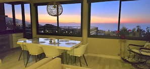 A dining area with a table and chairs, large windows with a view of the sea and mountains, and a hanging light fixture. - Villa with Privacy and Spectacular Views of Teide, Sea, Orotava Valley (La Orotava)