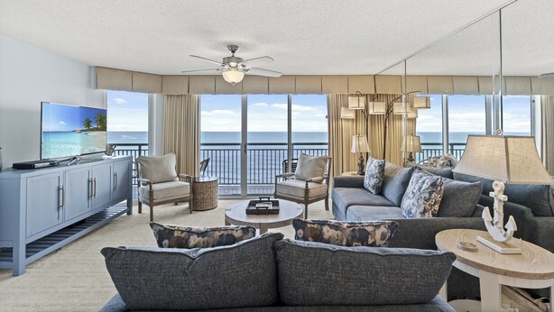 A spacious living room with a large flat-screen TV, comfortable seating, a ceiling fan, and a view of the ocean. - Oceanfront Windy Hill Beach 1K 3Q (North Myrtle Beach)