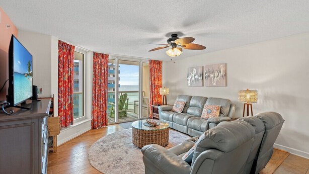 A spacious living room with a large sofa, a television, and a ceiling fan.