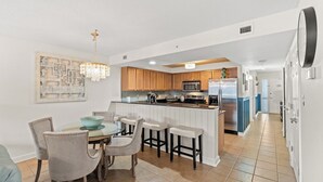 A modern kitchen with wooden cabinets, a central island with bar stools, a chandelier, and a dining area with a table and chairs.