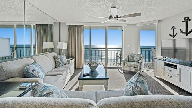 A modern hotel room with a balcony, a ceiling fan, a sofa, a coffee table, and a TV. - Luxurious 3-bedroom, 3-bathroom oceanfront condo, 7th floor views | Windy Hill Dunes - 703 (North Myrtle Beach)