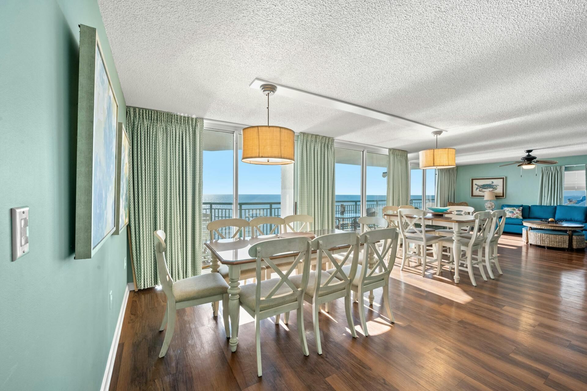 A spacious living area with a dining table and chairs, a blue sofa, and a balcony with a view of the ocean.