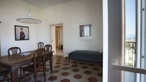 A room with a dining table, chairs, a bed, and a view through an open door. - Panoramic apartment with large roof terrace in Naples, view of harbor, Vesuvius (Neapel)